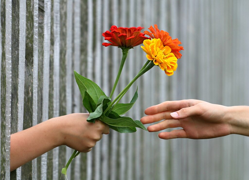 柵越しに手渡されている赤とオレンジと黄色の花束